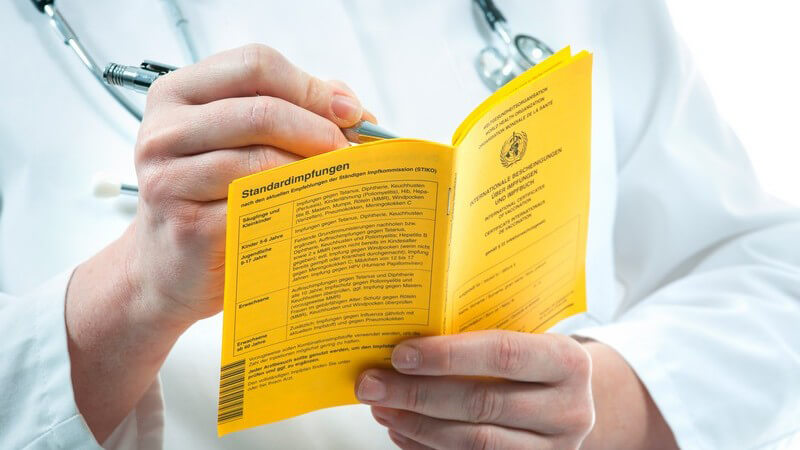 Arzt trägt etwas in einen gelben Impfausweis ein