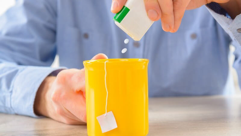 Tee in gelber Tasse wird mit Süßstoff gesüßt