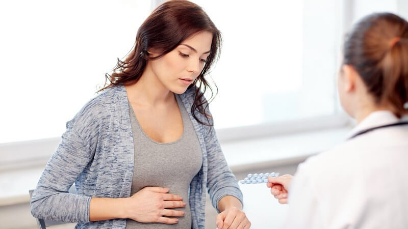 Ärztin im Krankenhaus überreicht einer schwangeren Frau mit Beschwerden einen Blister mit Tabletten