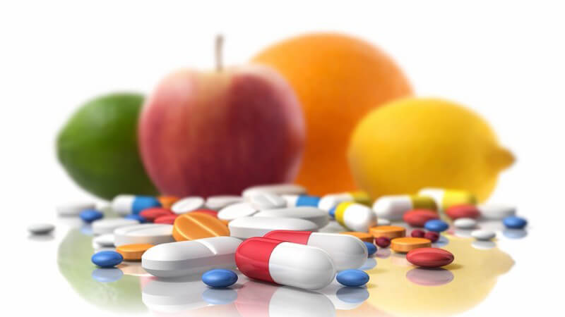Bunte Tabletten liegen vor verschiedenen Früchten