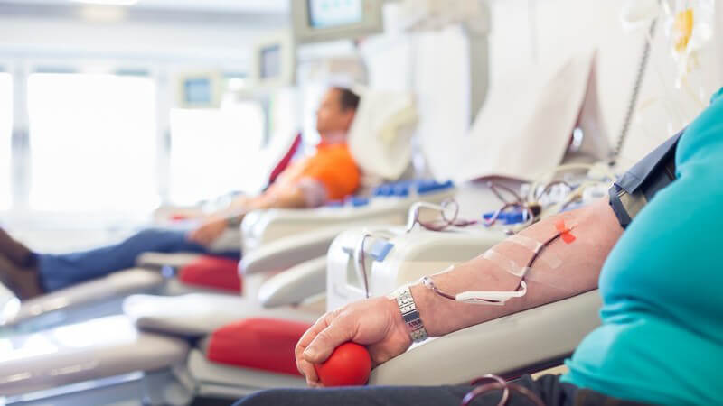 Frau mit rotem Ball in der Hand beim Blutspenden, im Hintergrund liegt ein weiterer Blutspender