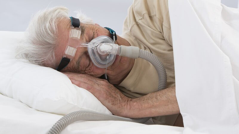 Alter Mann schläft im Bett mit aufgesetzter Atemmaske wegen Schlafapnoe