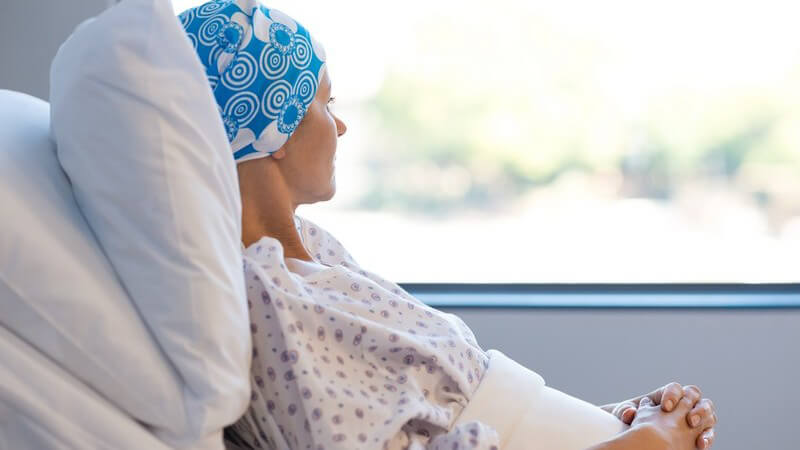 Krebspatientin liegt mit blauem Kopftuch im Krankenhausbett und guckt aus dem Fenster