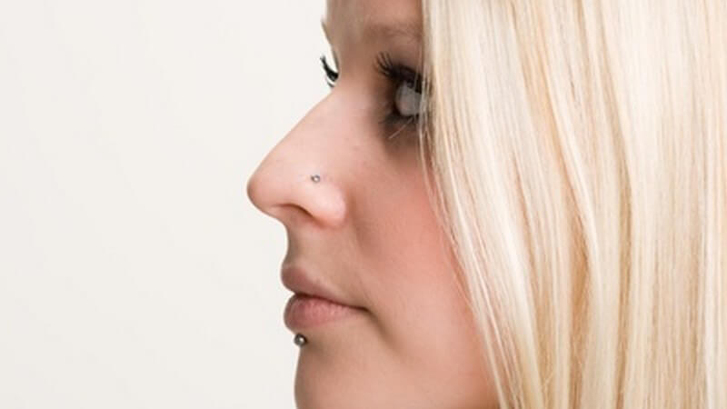 Seitliche Gesichtsaufnahme von junger blonder Frau mit Labret- und Nasenpiercing