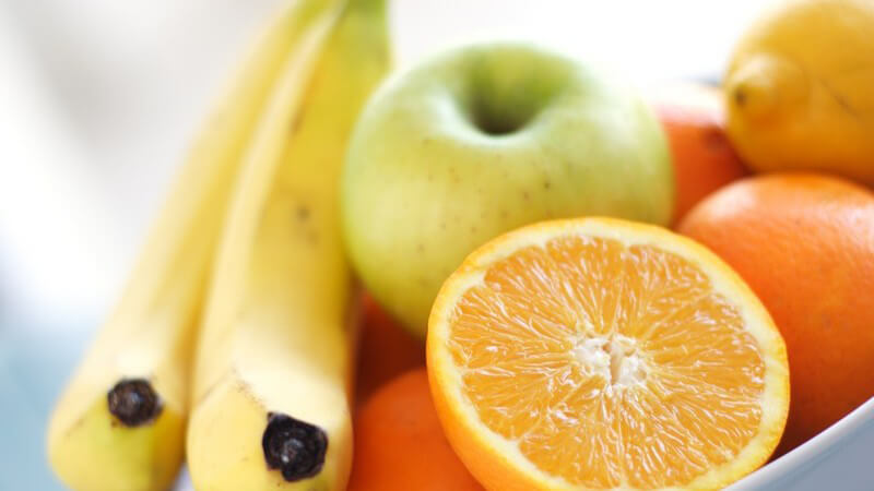 2 Bananen, ein Apfel, Orangen, Zitrone in weißer Schüssel