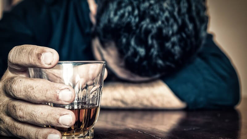 Alkoholproblem - Mann auf Tischplatte eingeschlafen, in der Hand ein Drink, Whiskey