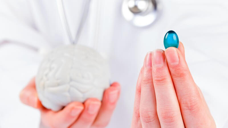 Arzt mit blauer Kapsel (Tablette) in den Fingern, in der anderen Hand ein graues Gehirn-Modell