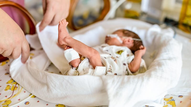 Versorgung eines in einem weißen Tuch liegenden Neugeborenen auf einem Wickeltisch