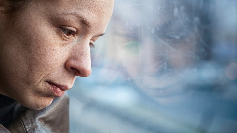 Einsame Frau sitzt traurig an die Scheibe eines Fensters gelehnt im Bus