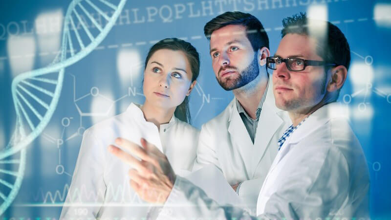 Drei Genetiker in weißen Kitteln stehen an einem Medienscreen