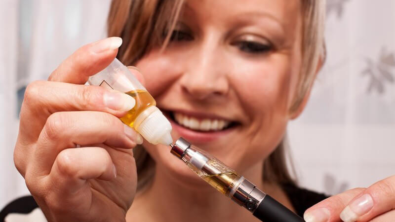Frau beim Befüllen einer E-Zigarette mit gelbem Liquid