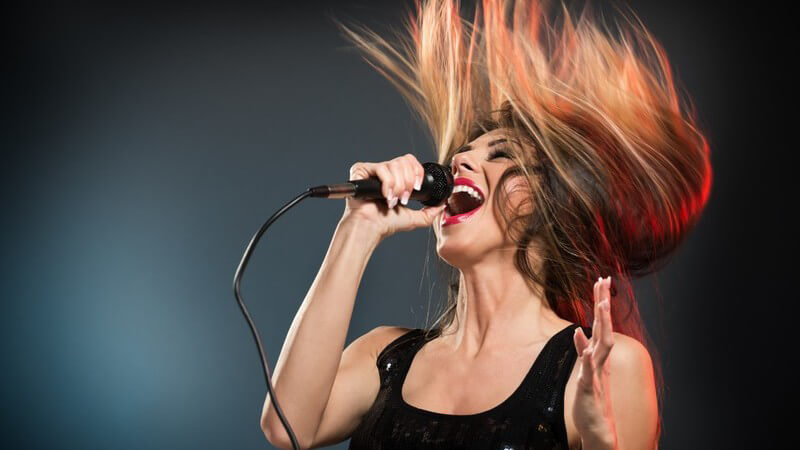 Sängerin in schwarzem Kleid vor dunklem Hintergrund, die Haare in die Luft gewirbelt