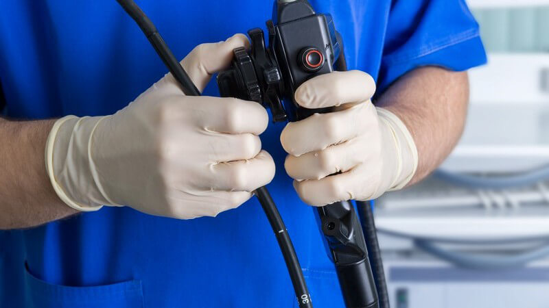 Arzt mit Gummihandschuhen und blauem Kittel hält ein Endoskop in den Händen