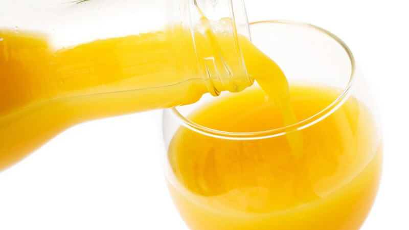 Orangensaft wird aus Glasflasche in Glas geschüttet