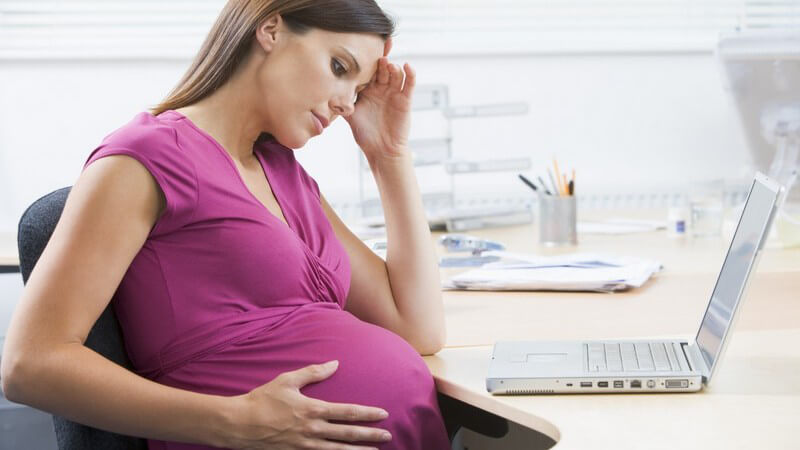 Schwangere Frau im Büro am Notebook guckt gestresst