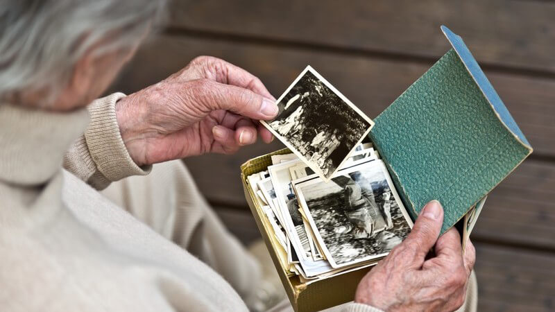 Erinnerungen an die Kindheit: alte Frau betrachtet Schwarz-Weiß-Fotos