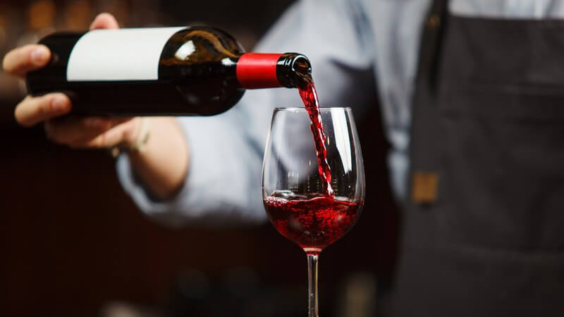 Kellner oder Weinsommelier mit Schürze schenkt einen Rotwein in ein Glas ein