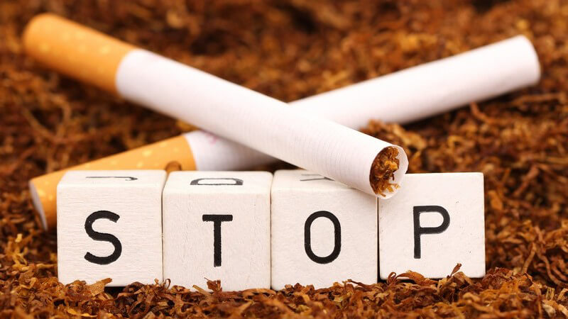 Vier Buchstabenwürfel bilden das Wort "STOP" auf einem Haufen Tabak und zwei Zigaretten