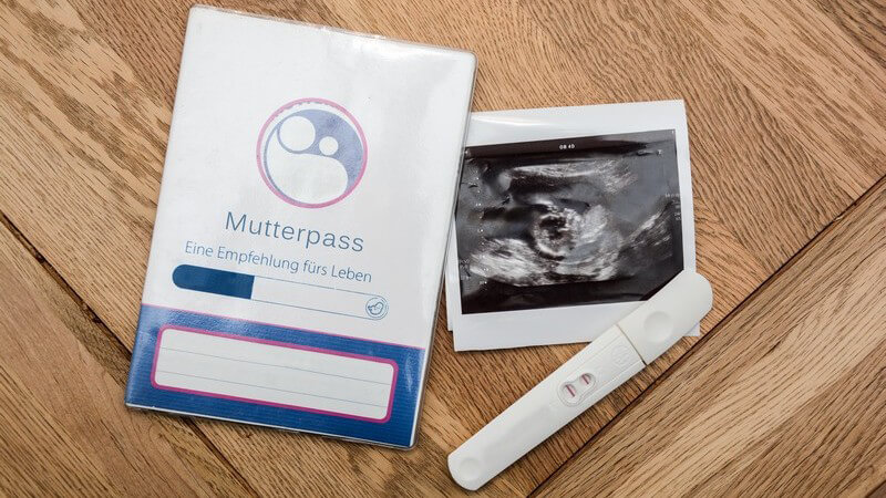 Mutterpass, Ultraschallbild und Schwangerschaftstest auf Holztisch