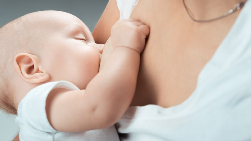 Mutter mit Halskette hält ihr Baby zum Stillen an die Brust