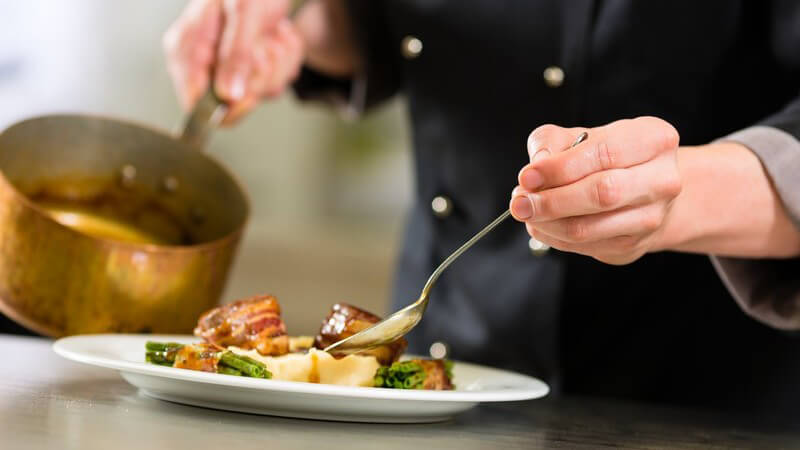 Teller mit Fleisch, Kartoffeln, Bohnen: Chefkoch im Restaurant oder Hotel gibt Sauce auf den Teller aus einem Topf