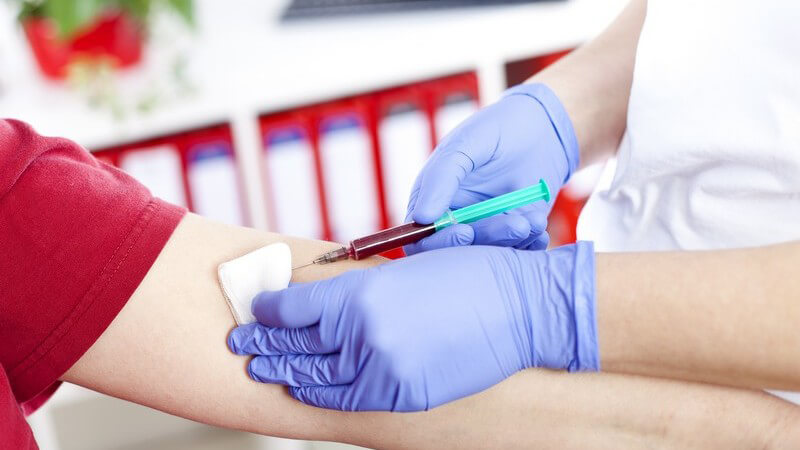 Blutabnahme mit Spritze am Arm in Arztpraxis