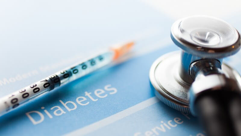 Stethoskop und Spritze auf einem blauen Blatt mit der Aufschrift "Diabetes"