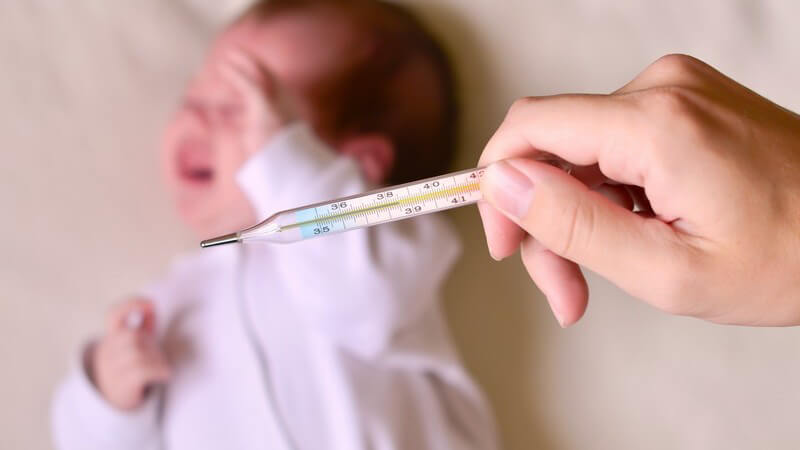Hand hält ein Fieberthermometer über einem schreienden Säugling