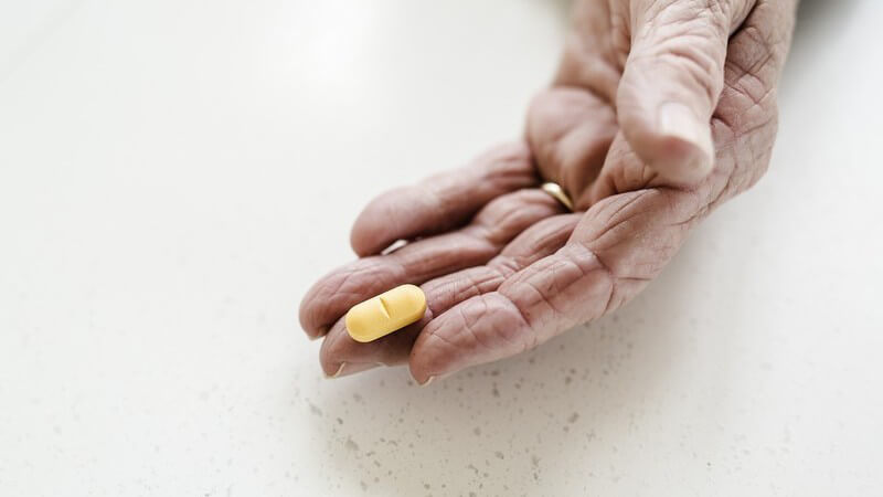 Hand einer alten Frau hält eine gelbe Tablette auf dem Mittelfinger