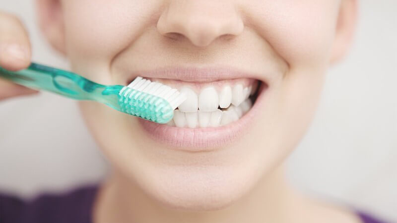 Frau putzt sich mit türkiser Zahnbürste die Zähne