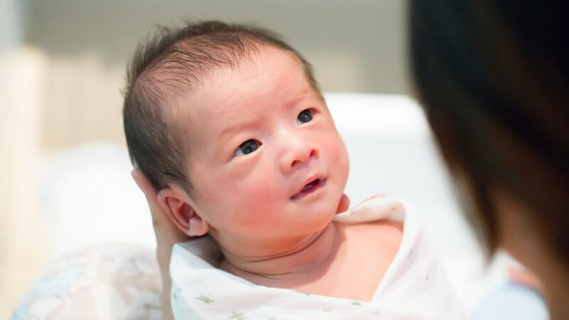 Asiatisches Baby mit schwarzen Haaren liegt eingewickelt in der Hand seiner Mutter