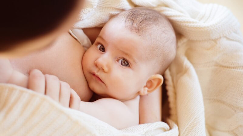 Baby schmiegt sich an der Brust ihrer Mutter und blickt in die Kamera