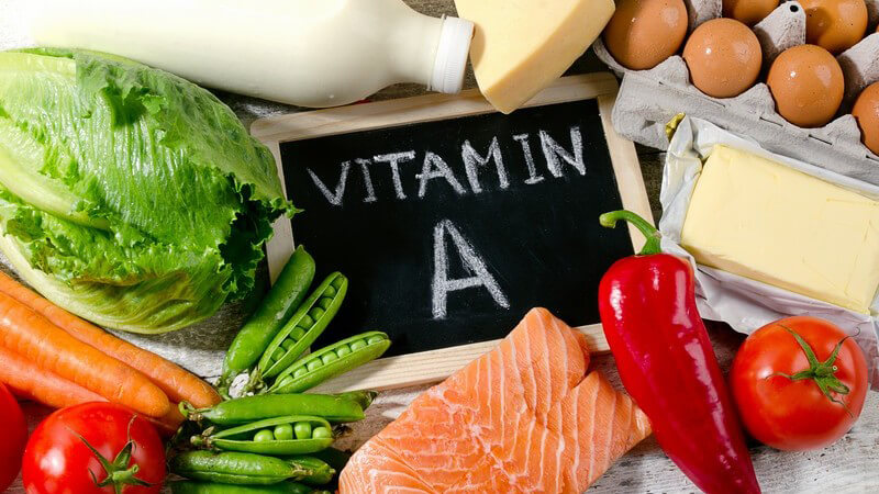 Vitamin A-haltige Nahrungsmittel wie Milch, Käse, Eier, Butter, Lachs, Tomaten und Möhren, mit Beschriftung auf Tafel