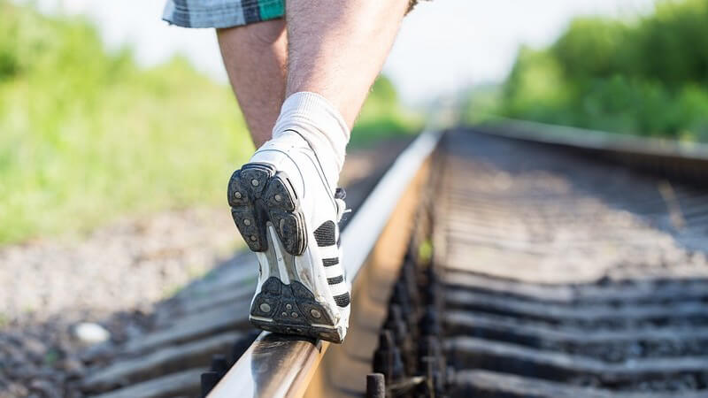 Mann in kurzer Hose und Turnschuhen balanciert über ein Bahngleis