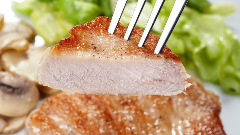 Nahaufnahme Gabel hält Stück Steak, Salat und Champignons als Beilage