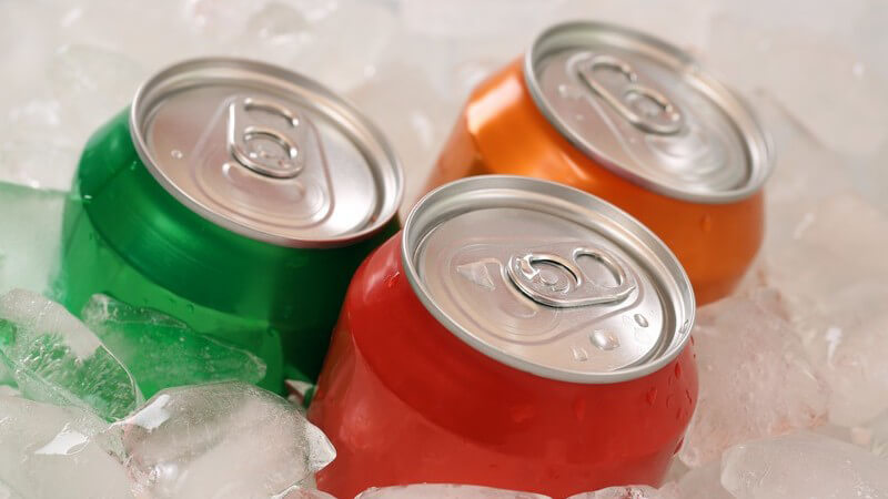 Drei farbige Getränkedosen (Cola und Limonade) umgeben von Eiswürfeln