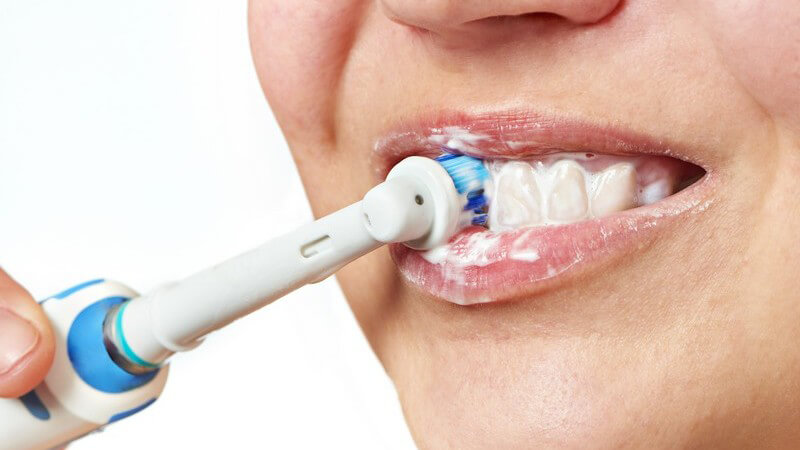 Frau putzt ihre Zähne mit einer elektrischen Zahnbürste vor weißem Hintergrund