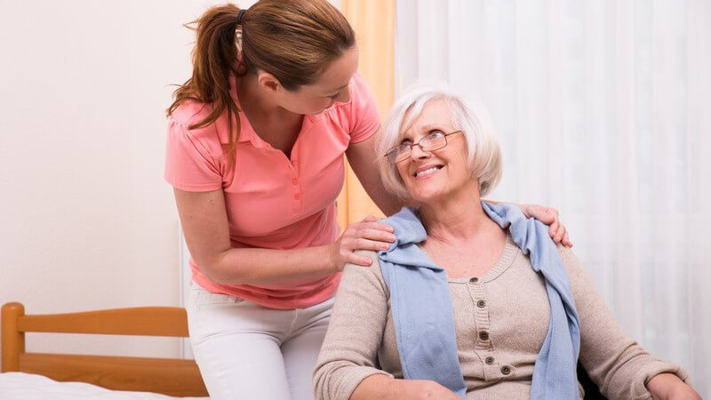 Pflegerin in rosa Poloshirt kümmert sich im Altenheim um eine ältere Dame im Rollstuhl
