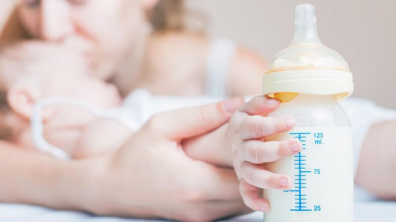Baby im Arm der Mutter hält ein Milchfläschchen in der Hand