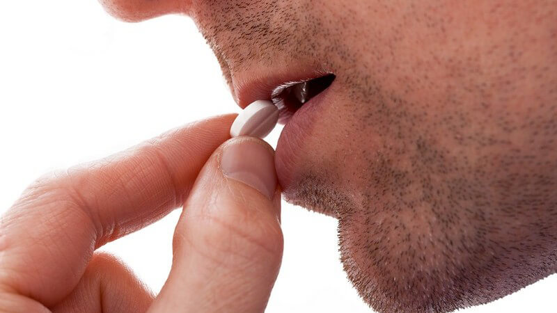 Mann mit Dreitagebart nimmt eine Tablette in den Mund