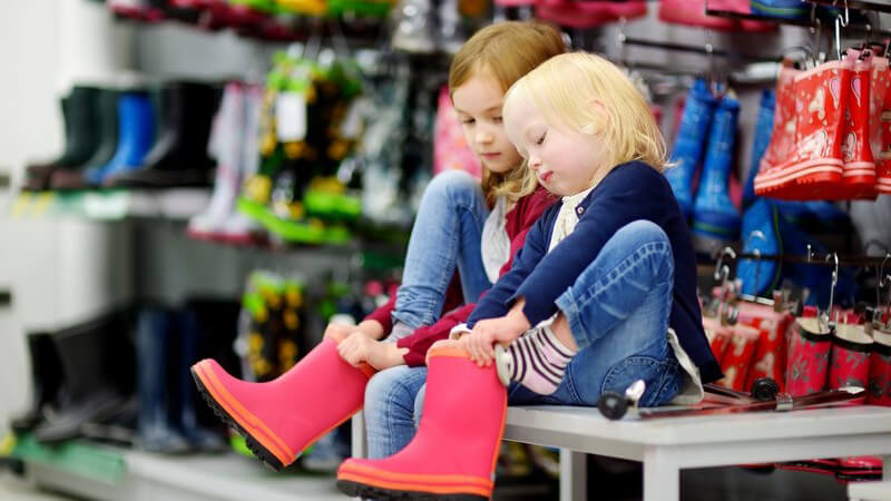 Zwei kleine Mädchen sitzen im Schuhgeschäft und probieren Gummistiefel an