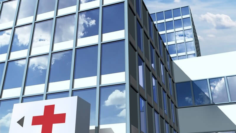 Krankenhaus mit spiegelnden Glasfronten und großem roten Kreuz