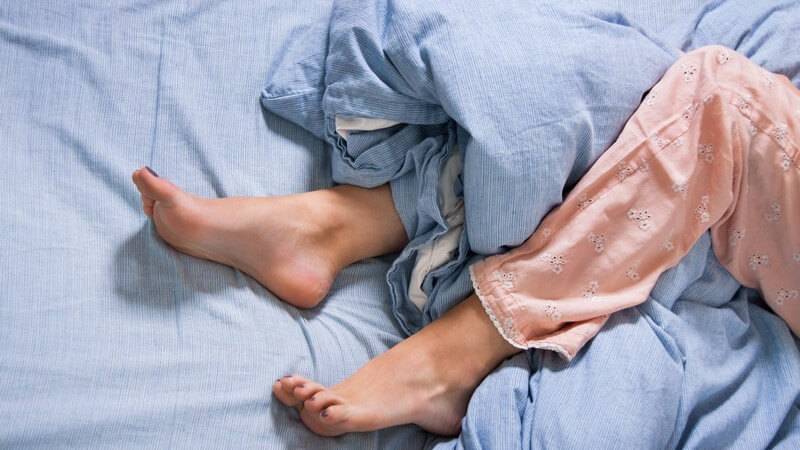 Beine und Füße einer Frau in rosa Schlafanzug in einem blauen Bett