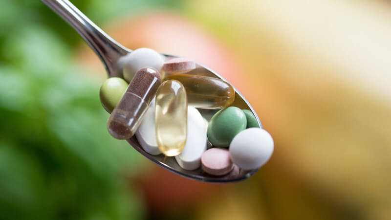 Esslöffel voller Pillen und Kapseln als Nahrungsergänzungsmittel, unscharfer Hintergrund