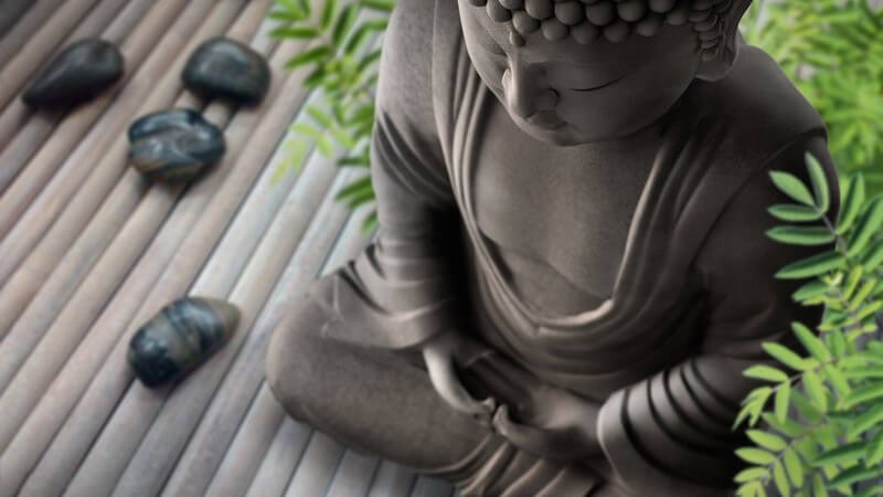Wellness: Buddhafigur auf Holzboden, daneben Steine und Bambuspflanze