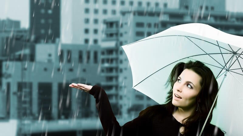 Dunkelhaarige Frau geht unter weißem Regenschirm an Regentag durch die Stadt