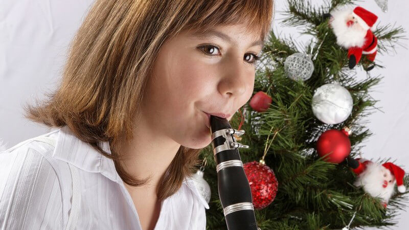 Kleines Mädchen spielt Klarinette vor dem Weihnachtsbaum