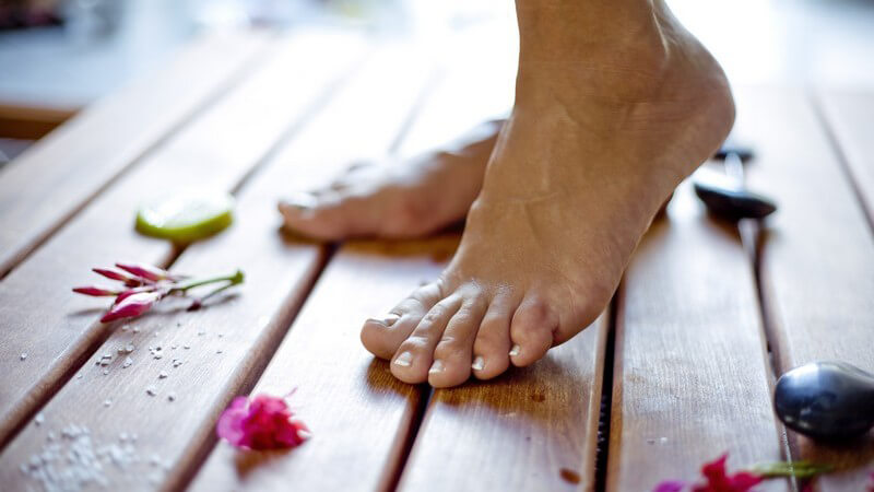 Wellness - Nackte Füße auf Holzboden mit Blüten und Lavasteinen