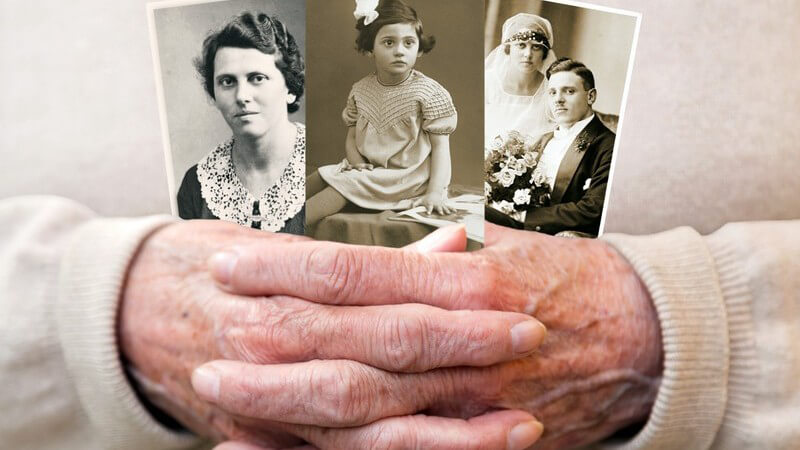 Gefaltete Seniorenhände halten drei alte schwarz-weiße Familienfotos
