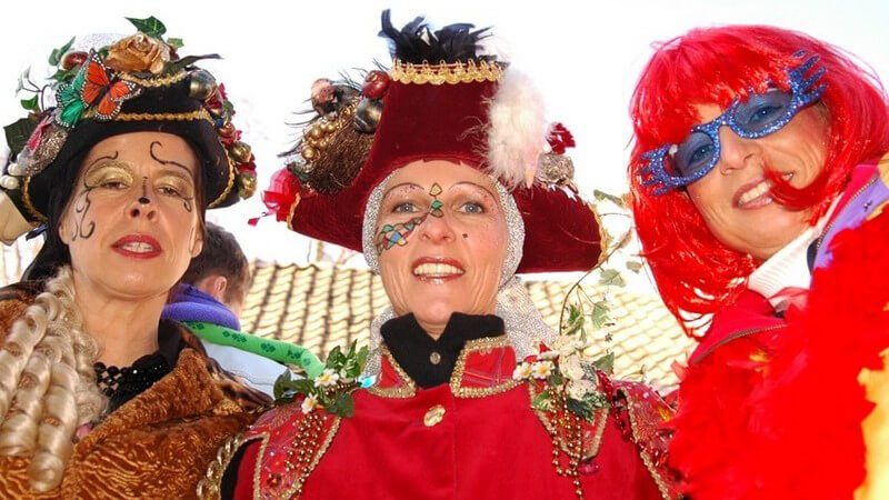 Drei reife jecke Frauen in Karnevalskostümen mit roter Perücke, Schminke, Hüten, Federn, Federboas